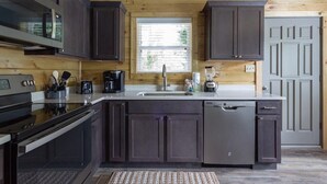 A modern kitchen with dark cabinets, stainless steel appliances, and a large window.