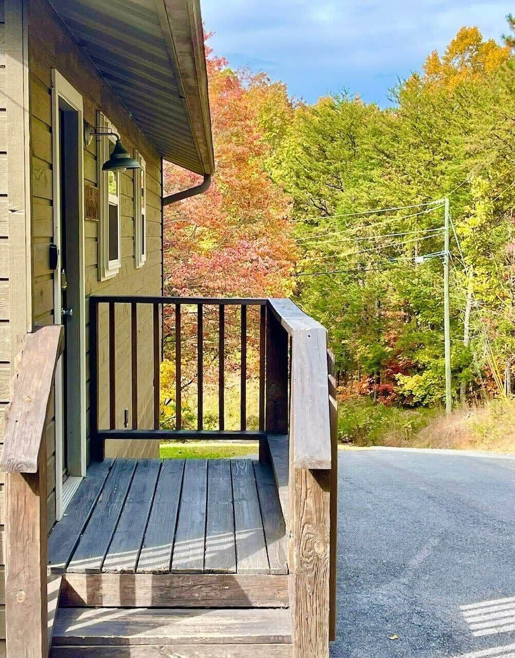 A wooden cabin with a porch and a view of autumn foliage.