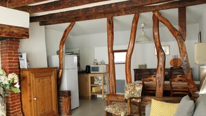A rustic interior with exposed wooden beams, a brick fireplace, a sofa with patterned cushions, and a dining area with wooden chairs and a table. - Detached house in an 18th-century property. (Mesnil-en-Ouche)