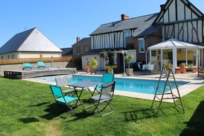 Un patio trasero con piscina, un porche cubierto y un césped con mobiliario exterior.