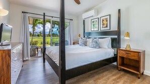 Een slaapkamer met een bed, een televisie, een nachtkastje en een balkon met uitzicht op groen.