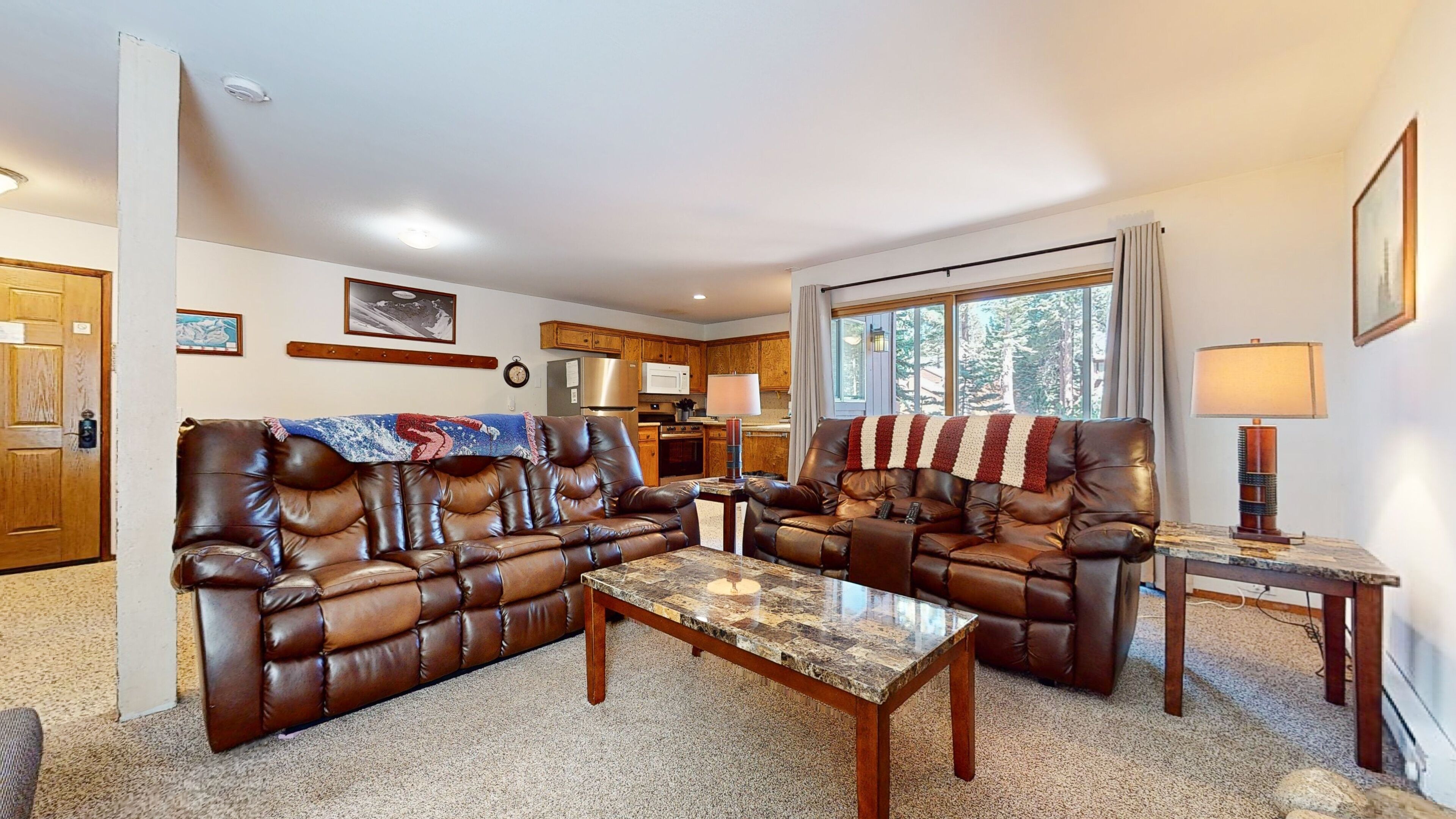 A living room with two brown leather sofas, a marble coffee table, and a kitchen in the background.