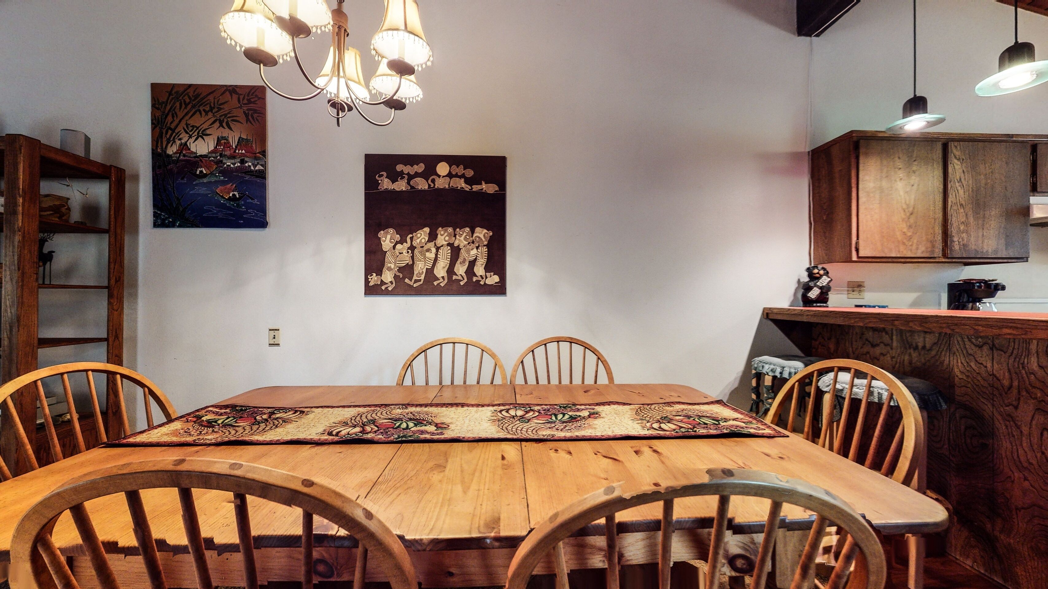 A dining area with a wooden table, four chairs, a chandelier, and artwork on the walls.