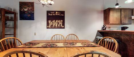 A dining area with a wooden table, four chairs, a chandelier, and artwork on the walls.