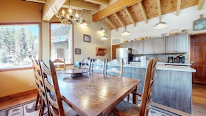 A wooden dining table with chairs, a kitchen with grey cabinets, and a view of trees outside. - Rainbow Villas 1 Charming Boutique complex, Dual Master Suites, Forest Mountain Views by RedAwning (Mammoth Lakes)
