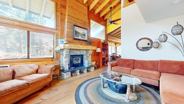 A cozy living room with a stone fireplace, wooden beams, and a large window. - Rainbow Villas 1 Charming Boutique complex, Dual Master Suites, Forest Mountain Views by RedAwning (Mammoth Lakes)