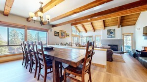 A spacious dining area with a large wooden table and chairs, a fireplace, and large windows offering views of the outdoors. - Val DIsere 10 5-Star Luxury with Game room and Gorgeous Mountain Views, Walk to The Village. by RedAwning (Mammoth Lakes)