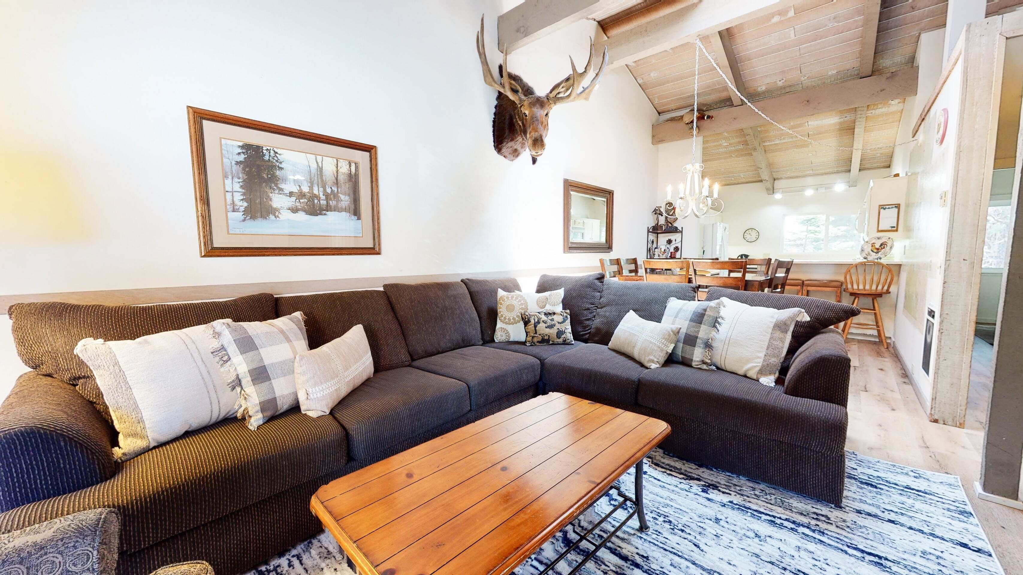 Un salon chaleureux avec un canapé d’angle, une table basse en bois et une tête de cerf accrochée au mur.