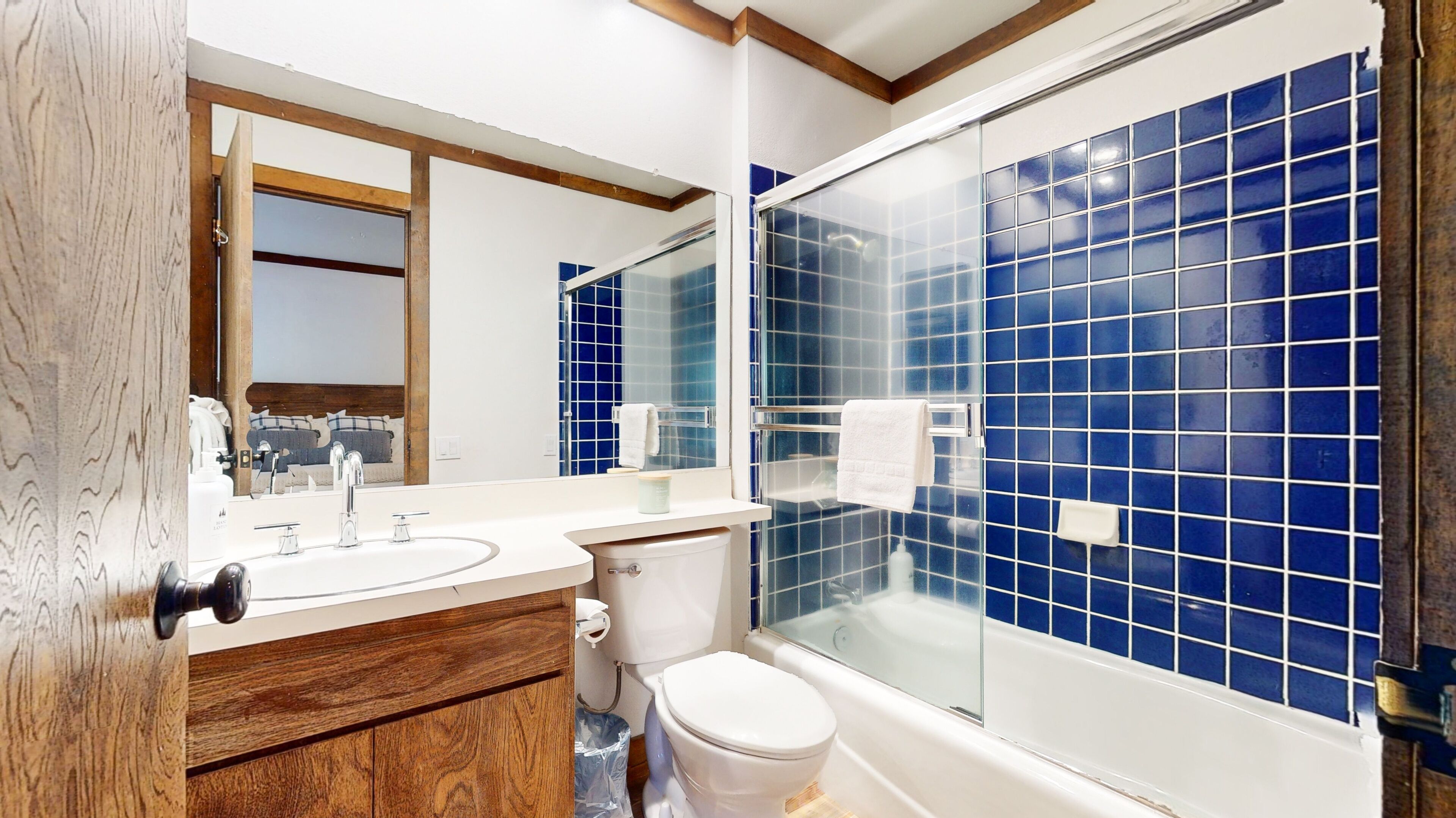 Ein modernes Badezimmer mit Waschbecken, Holz-Badmöbel, Toilette und einer Duschkabine mit blauen Fliesen.