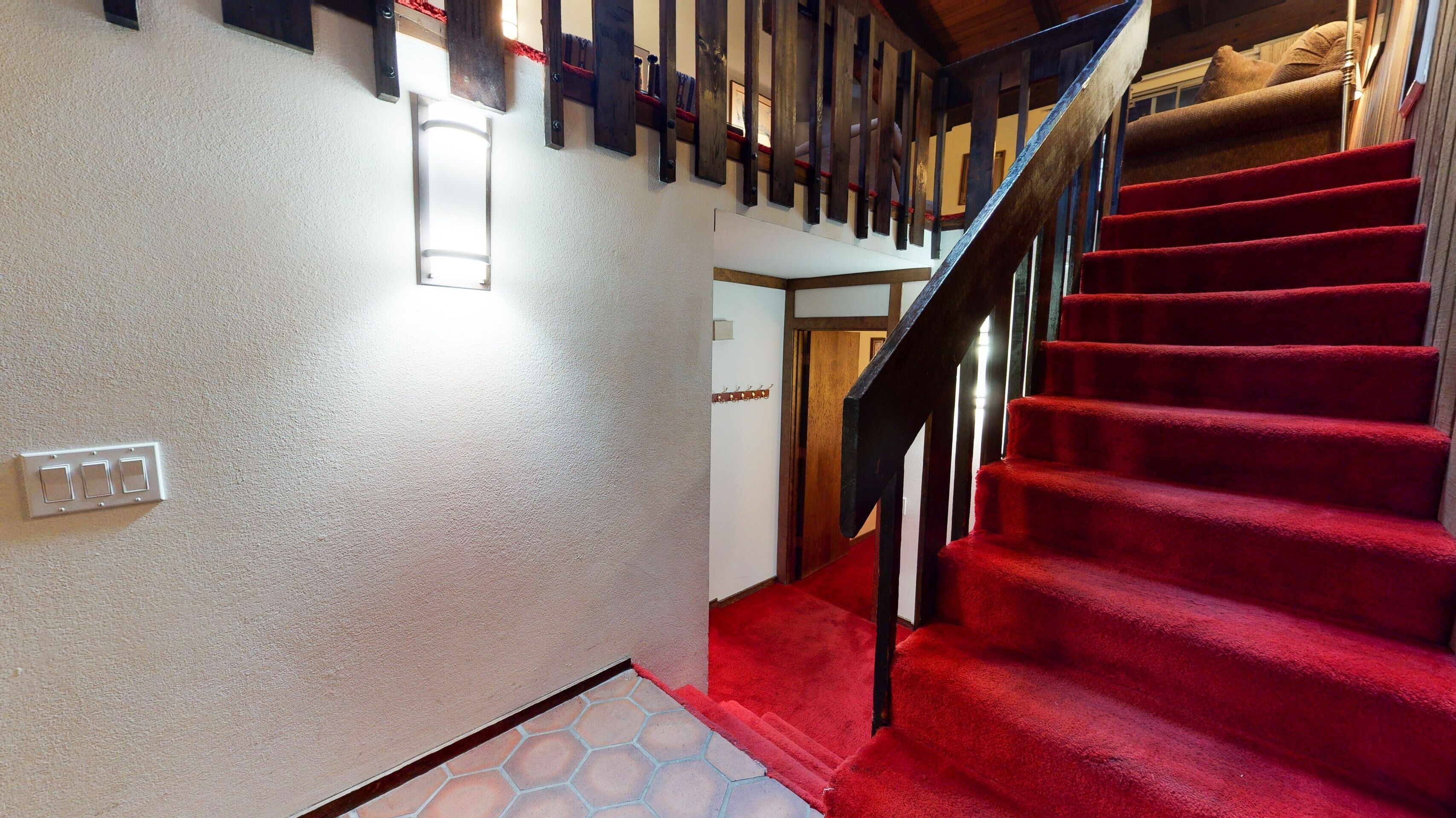 Una scala con tappeto rosso che conduce al secondo piano, ringhiere in legno e un lampadario a parete.