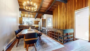 A spacious dining area with a long wooden table and chairs, a chandelier, and a rustic wooden wall.