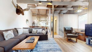 A modern living room with a sectional sofa, a coffee table, a television, and a mounted deer head.