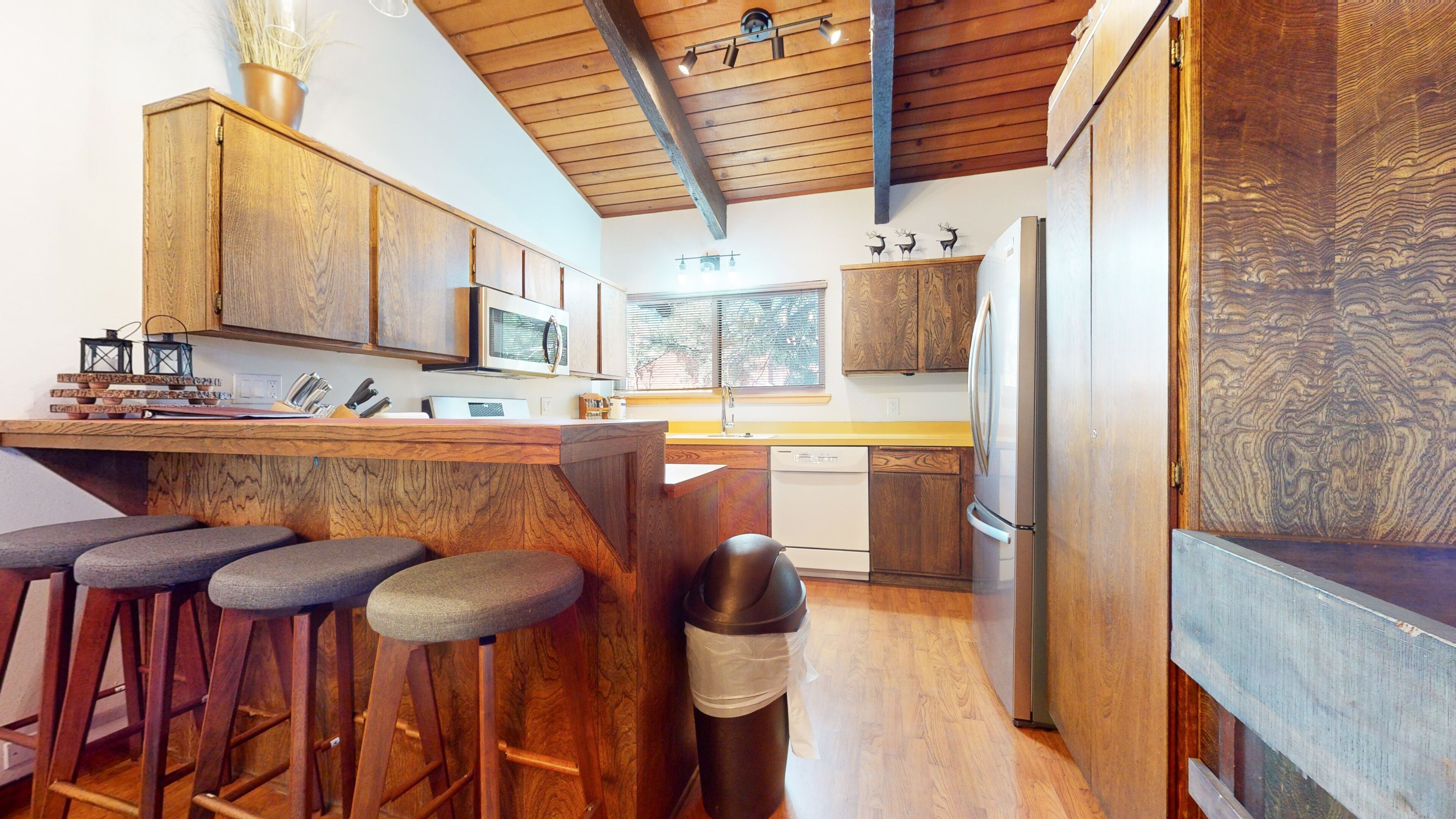 A modern kitchen with wooden cabinets, a stainless steel refrigerator, and a bar area with stools.