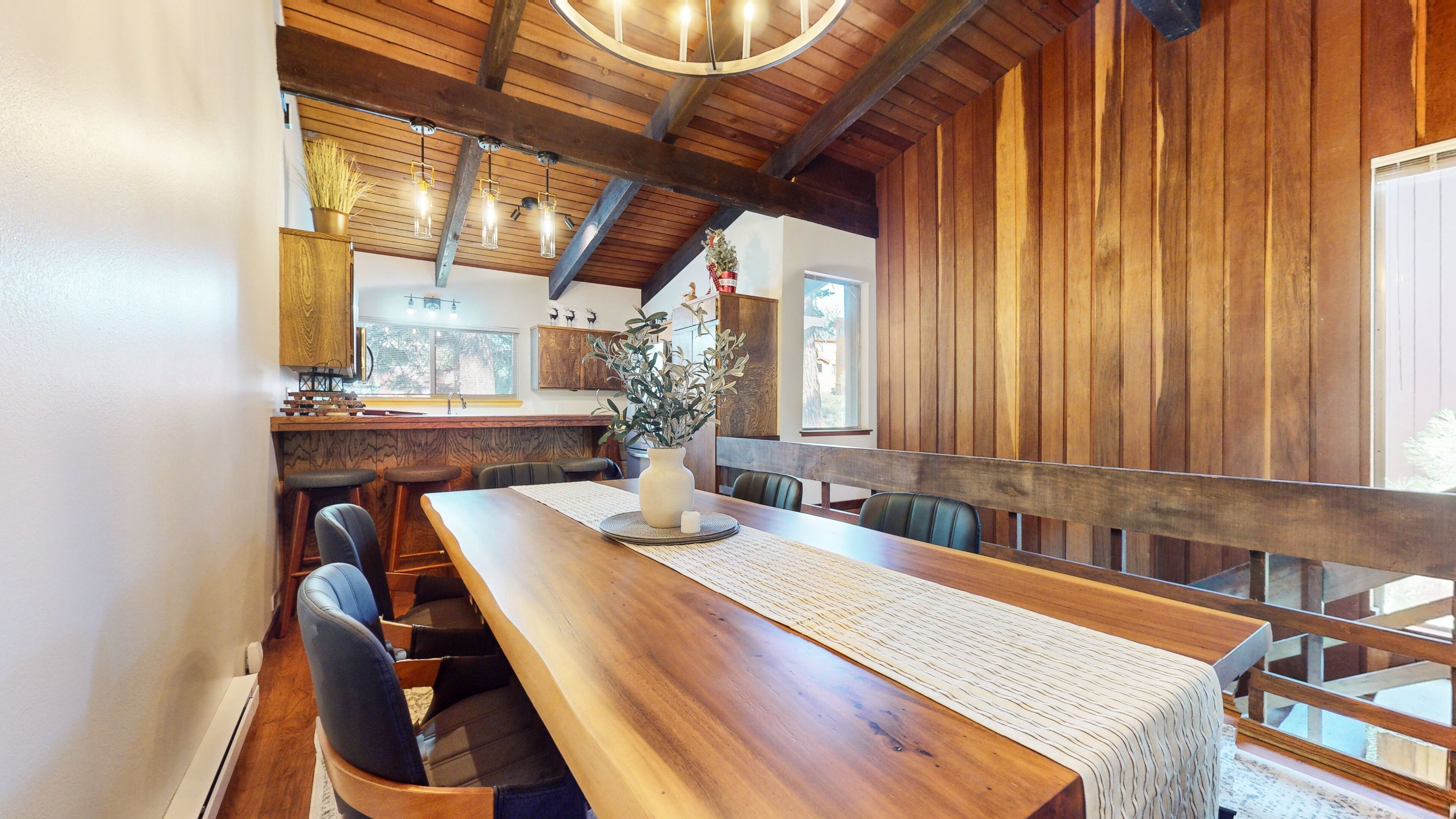 A wooden dining area with a long table, chairs, and a vase of flowers.