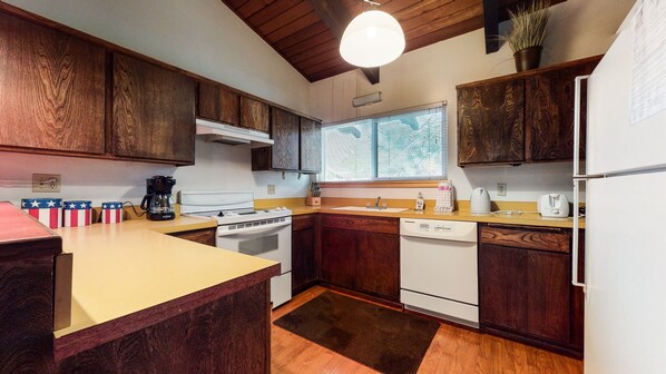 A kitchen with wooden cabinets, a stove, a dishwasher, and a window with blinds.