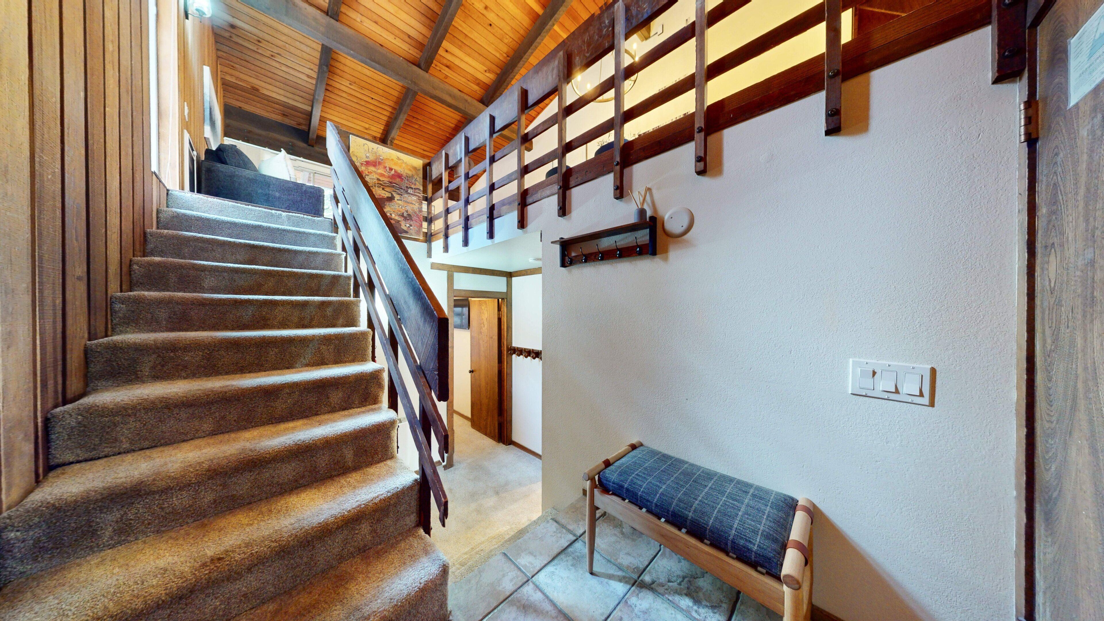 A staircase with wooden railings, a bench with a cushion, and a wall-mounted light fixture.