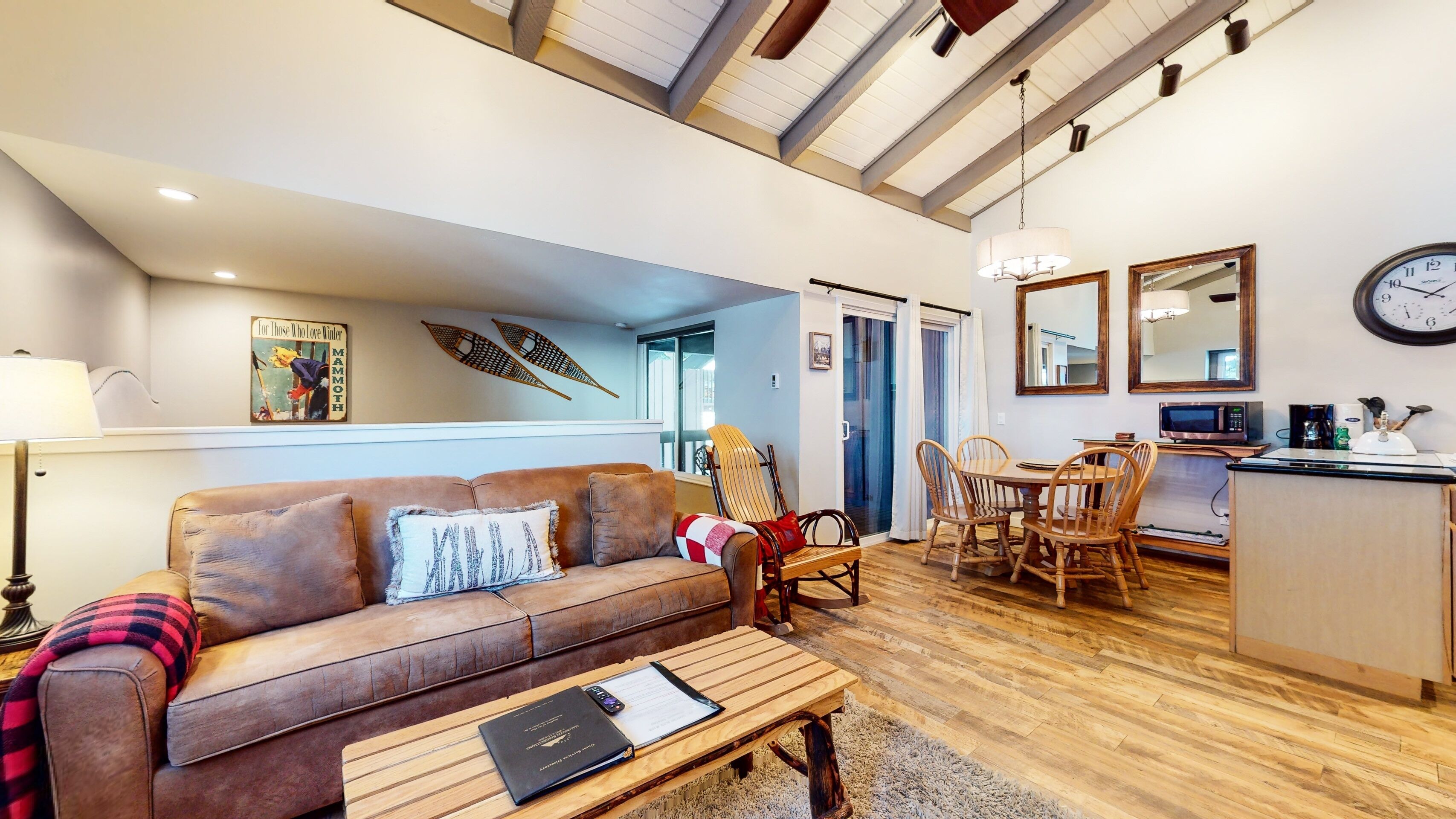 A cozy living room with a brown leather sofa, wooden coffee table, and a dining area with a wooden table and chairs.