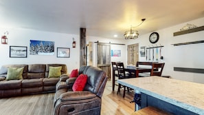 A cozy living room with a leather sofa, a dining area with a wooden table, and a kitchen counter.