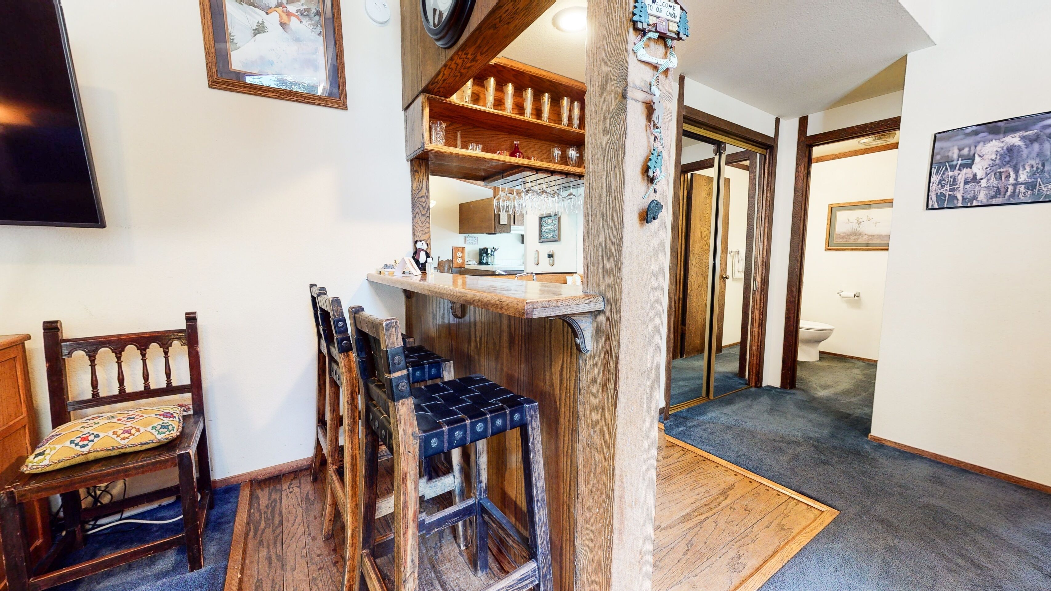 A wooden staircase with a bench, a wooden shelf with glassware, and a door leading to a bathroom.