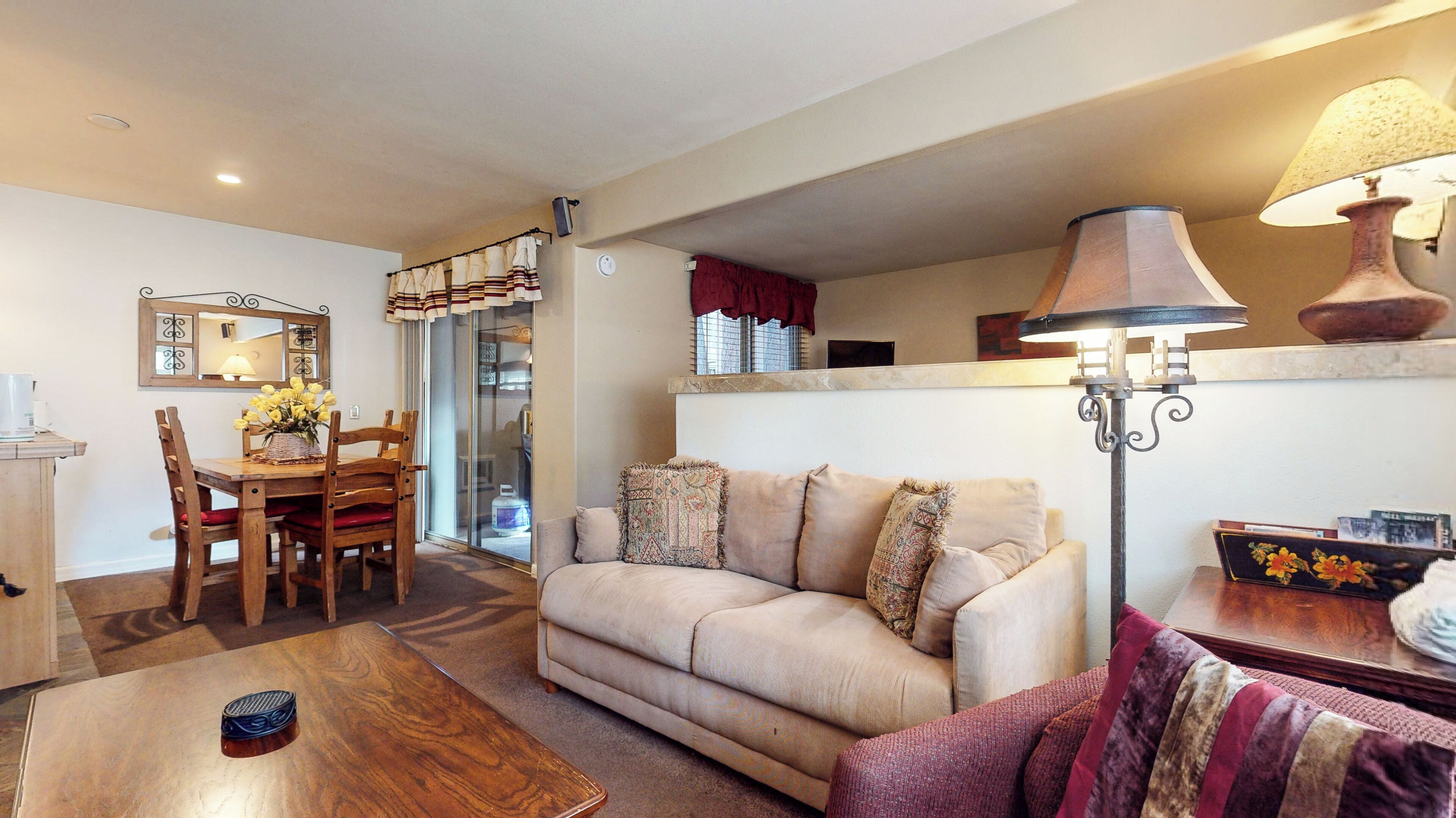 A living room with a beige sofa, wooden coffee table, and a dining area with a wooden table and chairs.