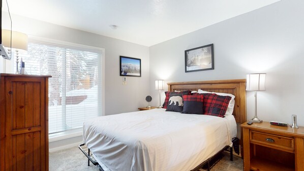 A bedroom with a large bed, two bedside tables, a wooden nightstand, a lamp, and a picture frame on the wall.