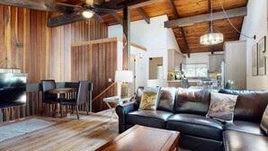 Un amplio salón con sofá de cuero, piso de madera y ventilador de techo.