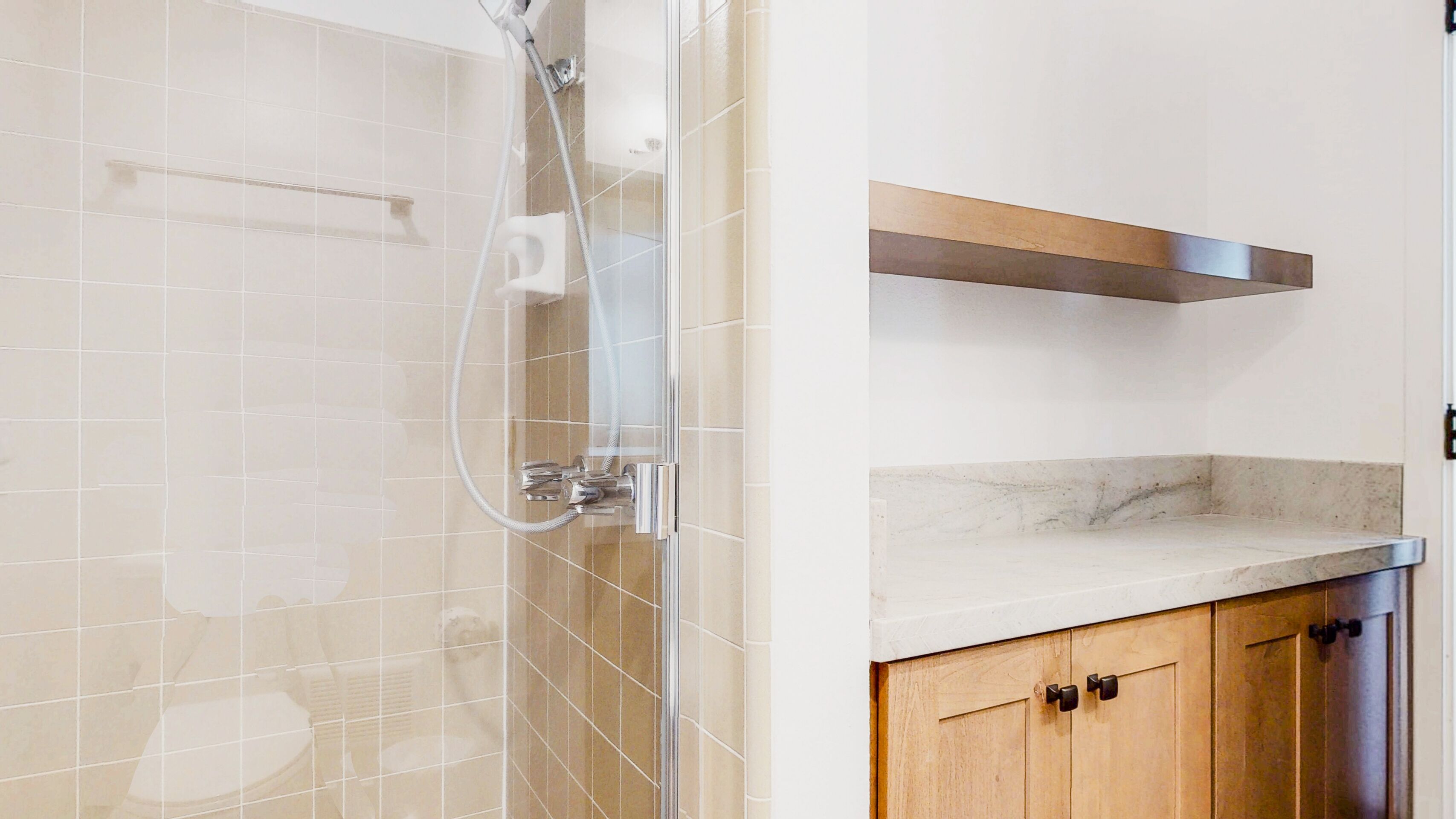 Un baño moderno con cabina de ducha de vidrio, encimera de mármol y muebles de madera.
