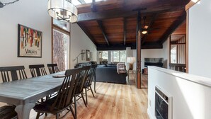Un comedor amplio con una mesa larga y sillas, una zona de cocina con sofá, y un ventanal que proporciona luz natural.