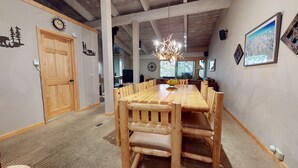 Un espace repas comprenant une longue table en bois et des chaises, un lustre et une grande fenêtre donnant sur un beau paysage.