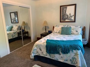 A bedroom with a bed, a nightstand, a lamp, a mirror, and a framed picture on the wall.