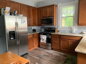 A kitchen with wooden cabinets, stainless steel appliances, a granite countertop, and a window with a view of greenery.