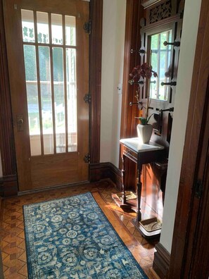 A wooden door with glass panels, a blue patterned rug, a small table with a potted plant, and a white wall with a decorative molding.