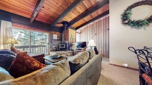 Un salon confortable avec une cheminée, un canapé, un téléviseur et une vue sur l’extérieur.