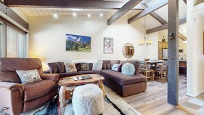 Uma sala de estar ampla com um sofá seccional grande, uma mesa de centro de madeira e um espaço de jantar com mesa e cadeiras de madeira.
