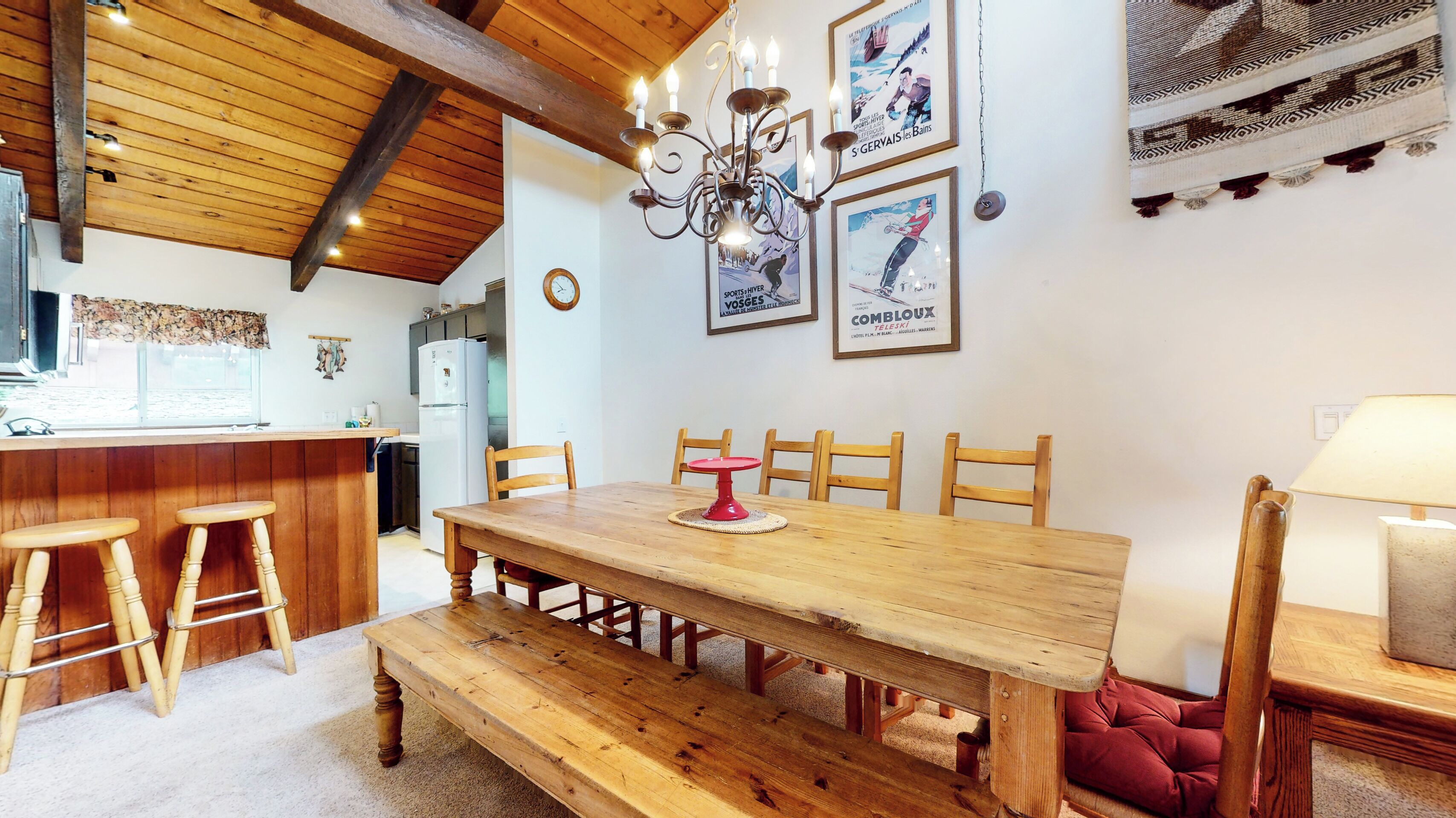 A wooden dining table with six chairs, a red cake stand, and a chandelier.