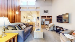A living room with a sofa, coffee table, TV, and a dining area with chairs and a table.