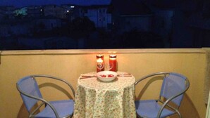 Un petit balcon avec une table et deux chaises, deux bougies et un saladier rempli de fruits.