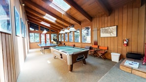 A pool table in a room with wooden walls and large windows.