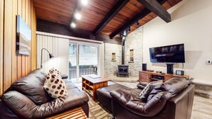 A cozy living room with leather sofas, a wooden coffee table, a stone fireplace, and a flat-screen TV. - Mountain Modern, Perfect for Summer, Near The Village, Pool On-site & Hot Tub (Mammoth Lakes)