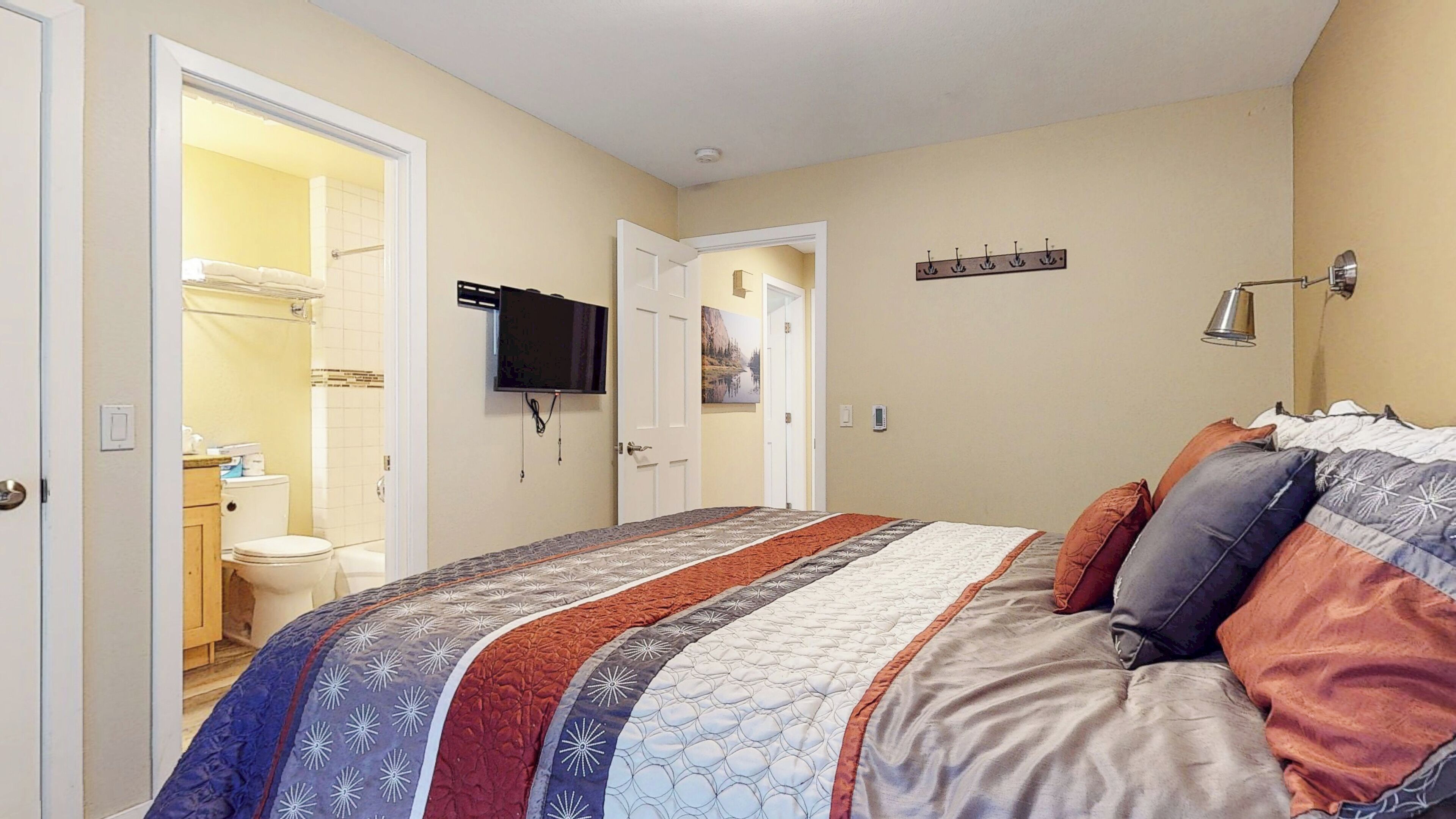 A bedroom with a bed, a television, a door leading to a bathroom, and a coat rack.