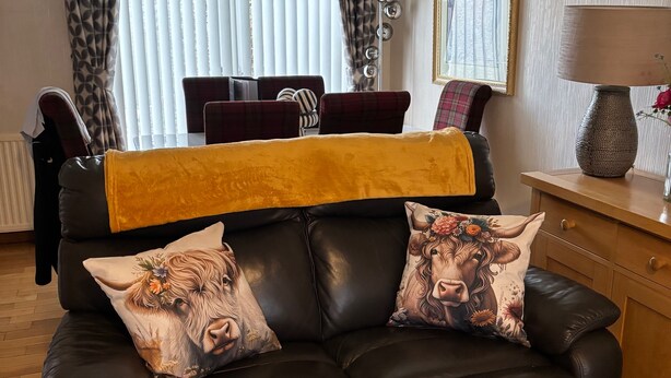A leather sofa with two decorative pillows, a yellow throw blanket, and a dining area with a table and chairs in the background. - 3bed House - Family Friendly - Close To Lochness (Inverness)