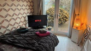 A bedroom with a bed, a TV displaying 'NETFLIX', a window with curtains, and a nightstand with a lamp. - 3bed House - Family Friendly - Close To Lochness (Inverness)