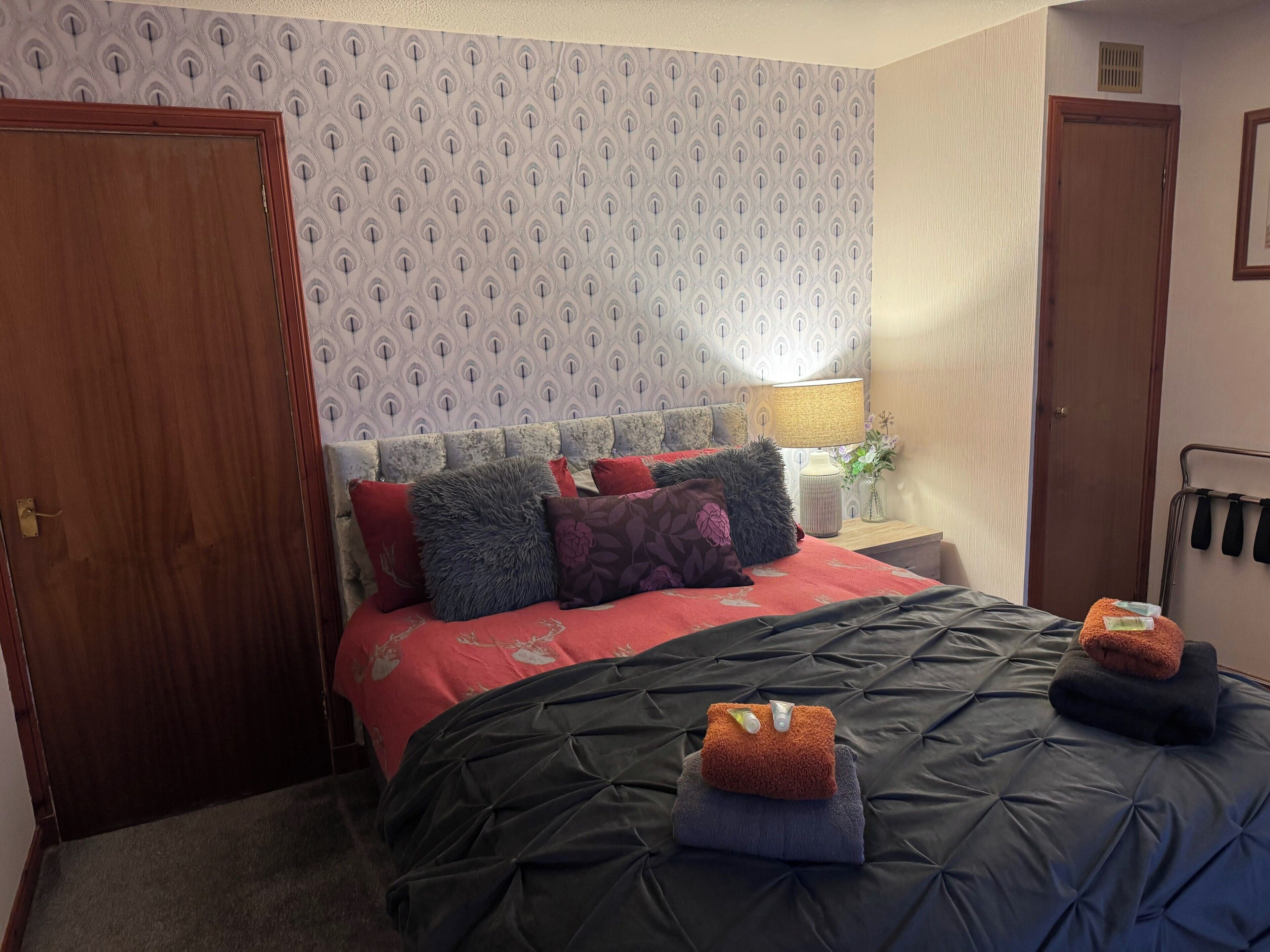 Una camera d'albergo con un letto grande, un comodino con una lampada e una parete con carta da parati decorata.