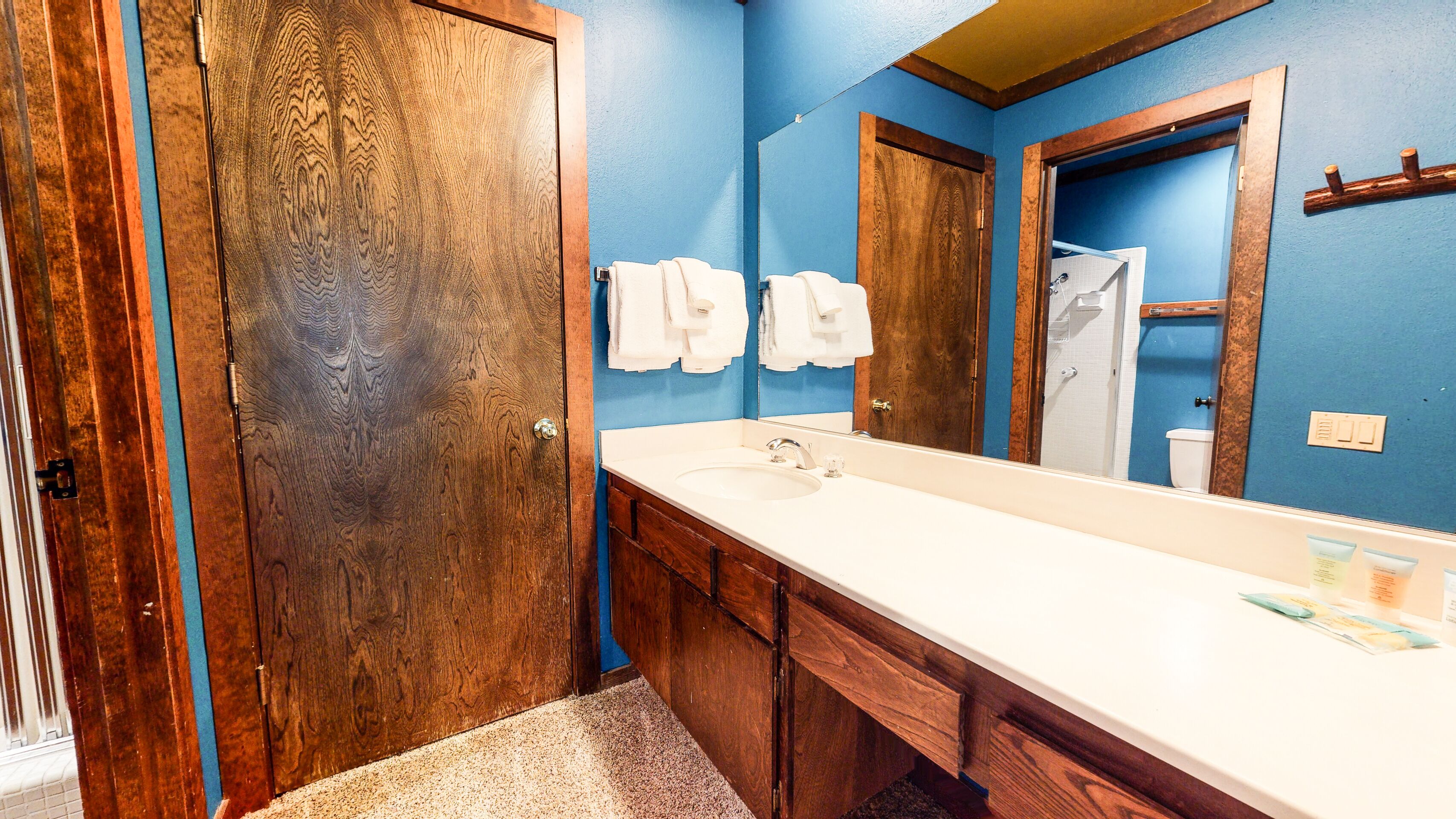 Un baño con una puerta de madera, un lavabo blanco y un espejo.