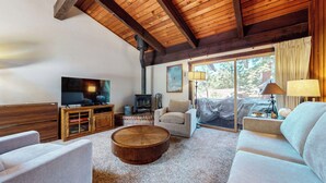 Un salon chaleureux avec un téléviseur, des meubles en bois, une cheminée et une grande fenêtre.
