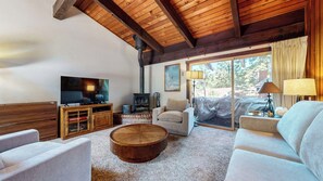 A cozy living room with a TV, wooden furniture, a fireplace, and a large window.