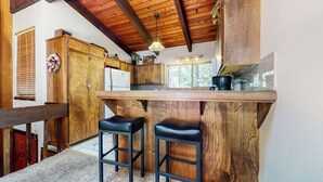 Une cuisine rustique avec des meubles de rangement en bois, un plan de travail, deux tabourets et un luminaire suspendu.