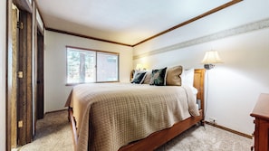 A bedroom with a bed, two bedside lamps, a window with blinds, and a door.