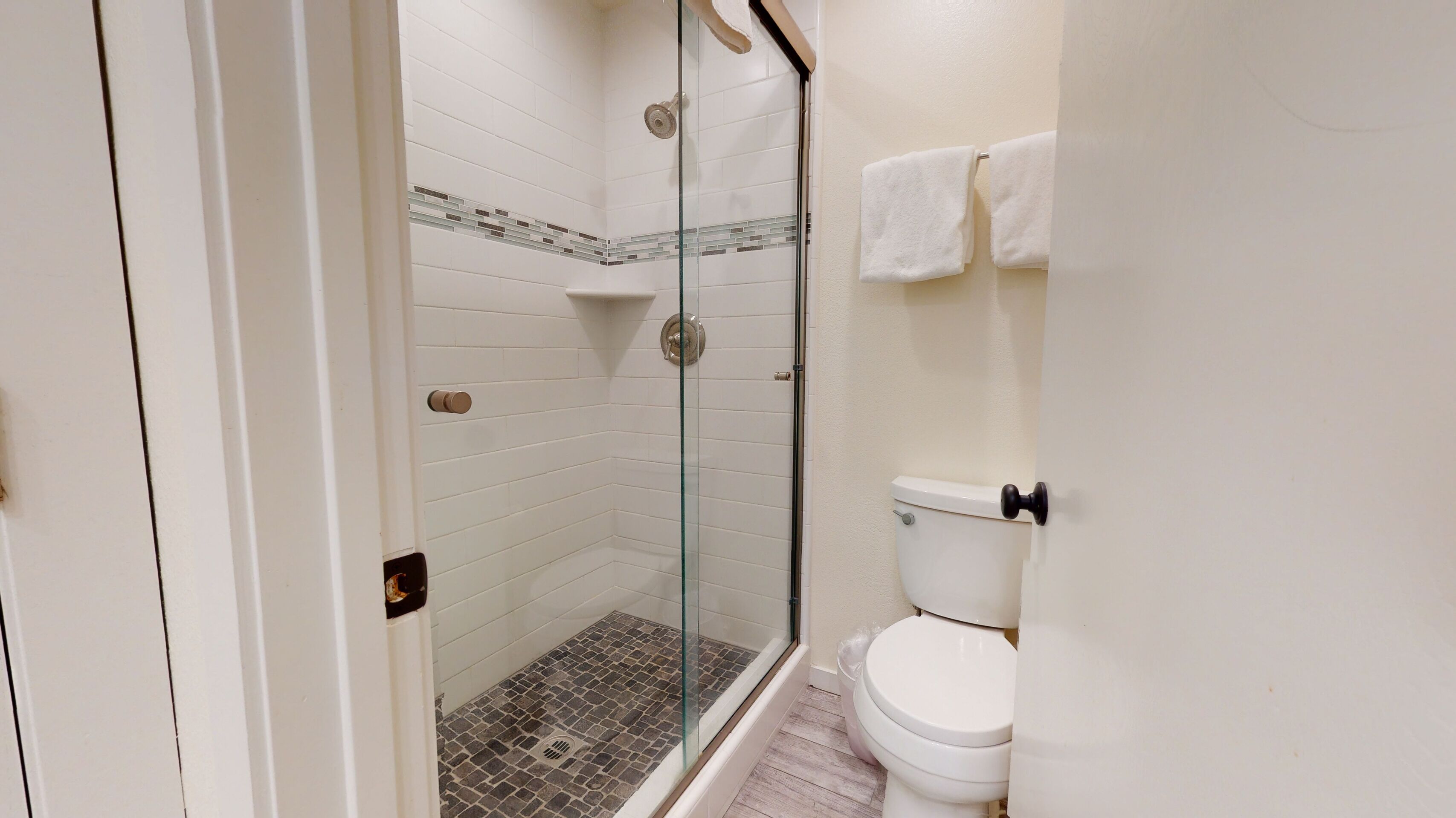 A bathroom with a glass-enclosed shower, white tiled walls, a toilet, and a towel rack.