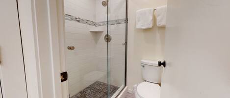 A bathroom with a glass-enclosed shower, white tiled walls, a toilet, and a towel rack.